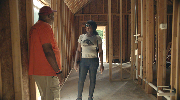 Kayla and man stand inside of a home that is being built